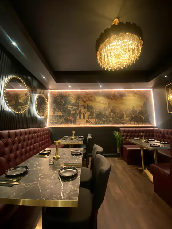 Oxblood booths beneath a chandelier and a backlit gold mural